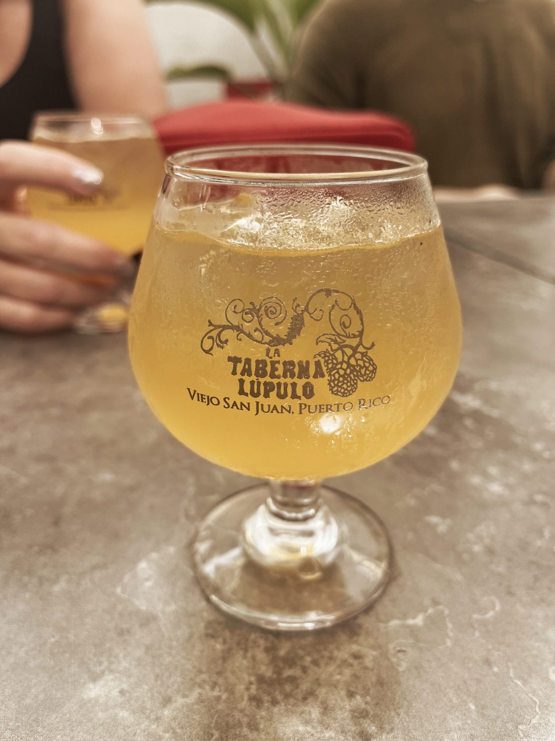 Two glasses of hazy beer on a stone table, one just set down, the other still in somebody's hand.