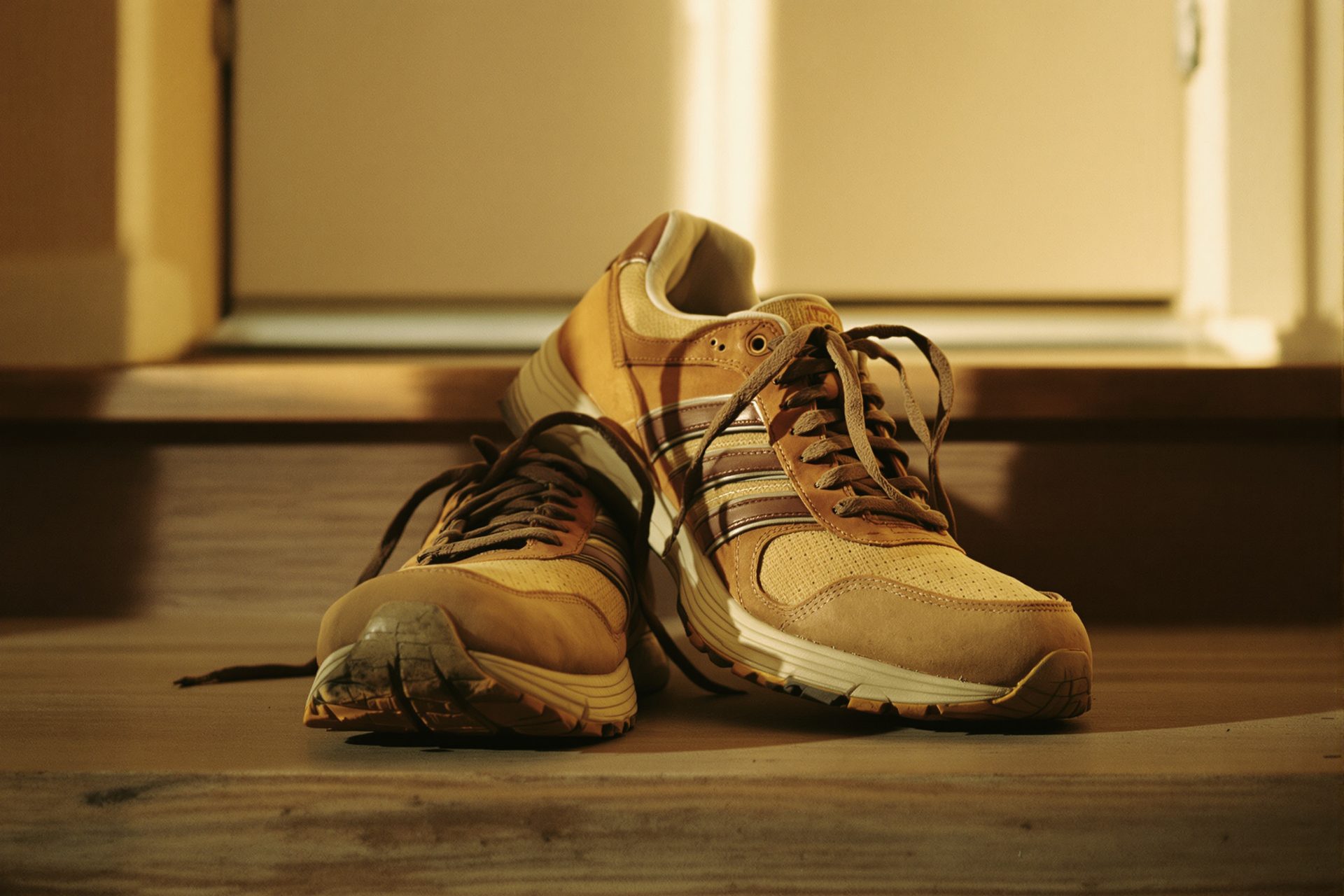 A pair of well-worn running shoes left on a doorstep in the morning light, laces loose and one tipped against the other.