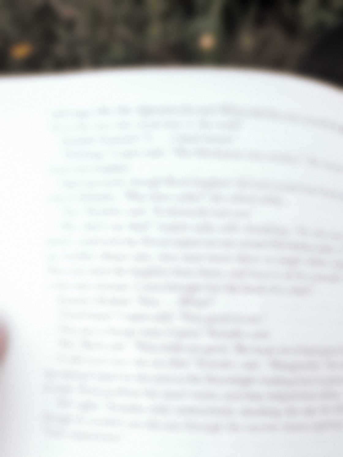 An open paperback held in one hand outdoors, the printed pages catching the light.
